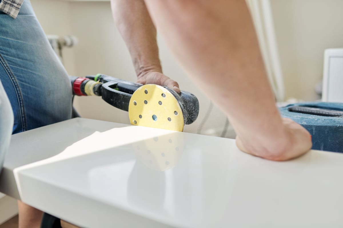 Orbital sander smoothing the edge of a white countertop during surface prep