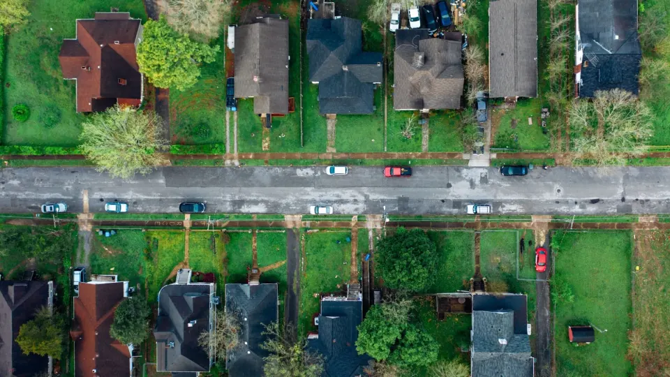 Overhead view of a residential street lined with houses, back gardens, and parked cars