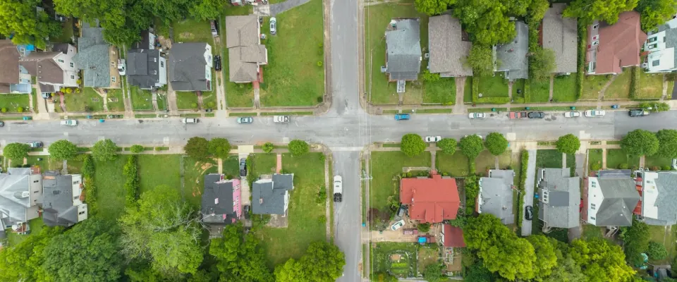 Overhead view of a tree-lined neighborhood crossroads with detached homes and green yards