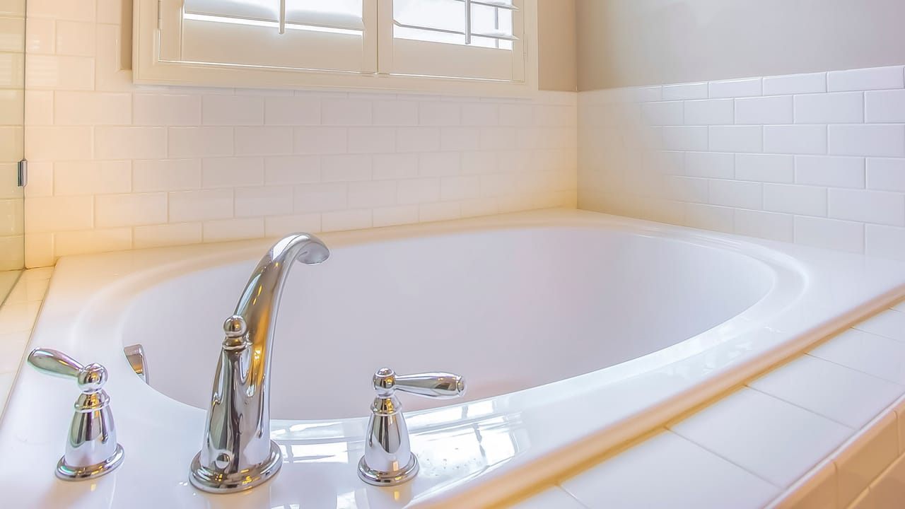 Refinished white drop-in bathtub with a glossy finish and polished chrome faucet against white subway tile