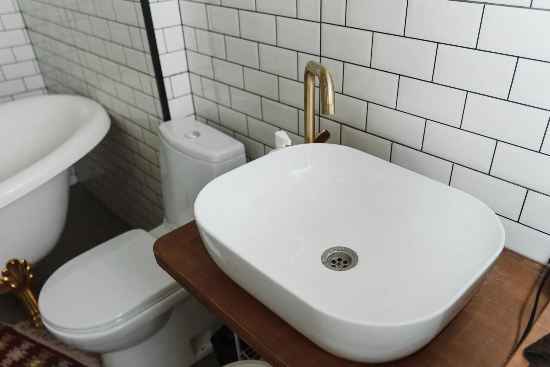 White vessel basin on a wood vanity with a clawfoot tub and subway tile behind it