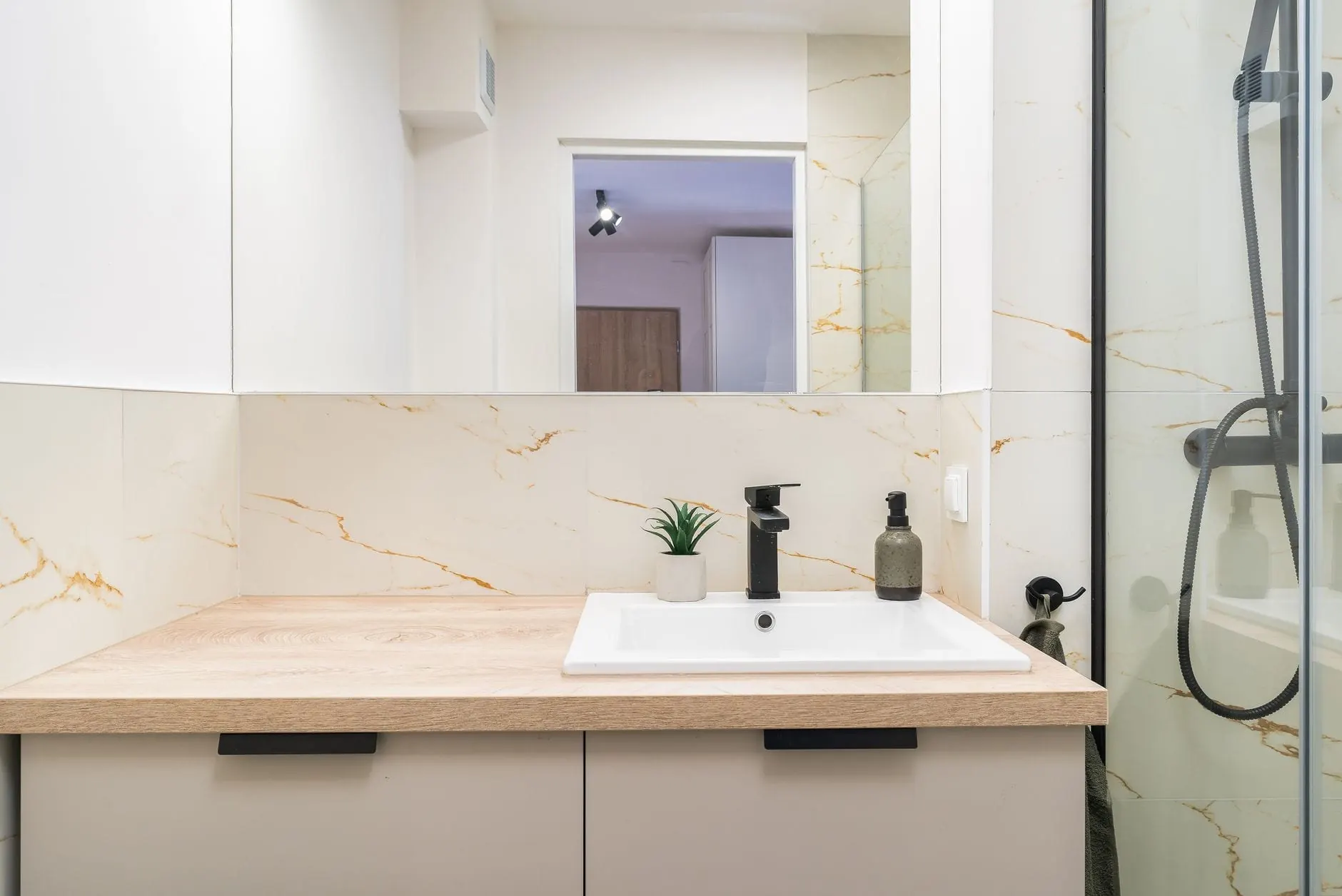 Compact vanity with a pale wood counter and a white drop-in basin beside a glass shower