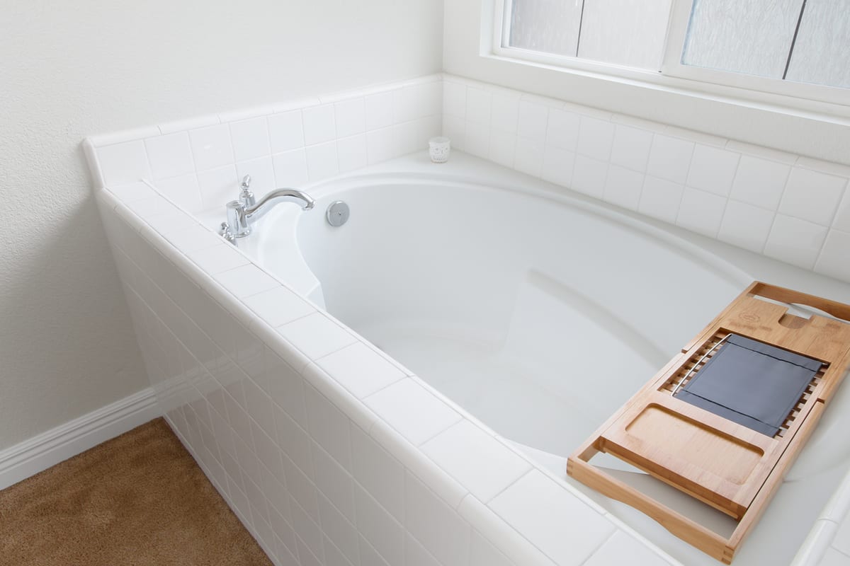 Refinished white alcove bathtub with a glossy basin, tiled surround, and a bamboo bath caddy
